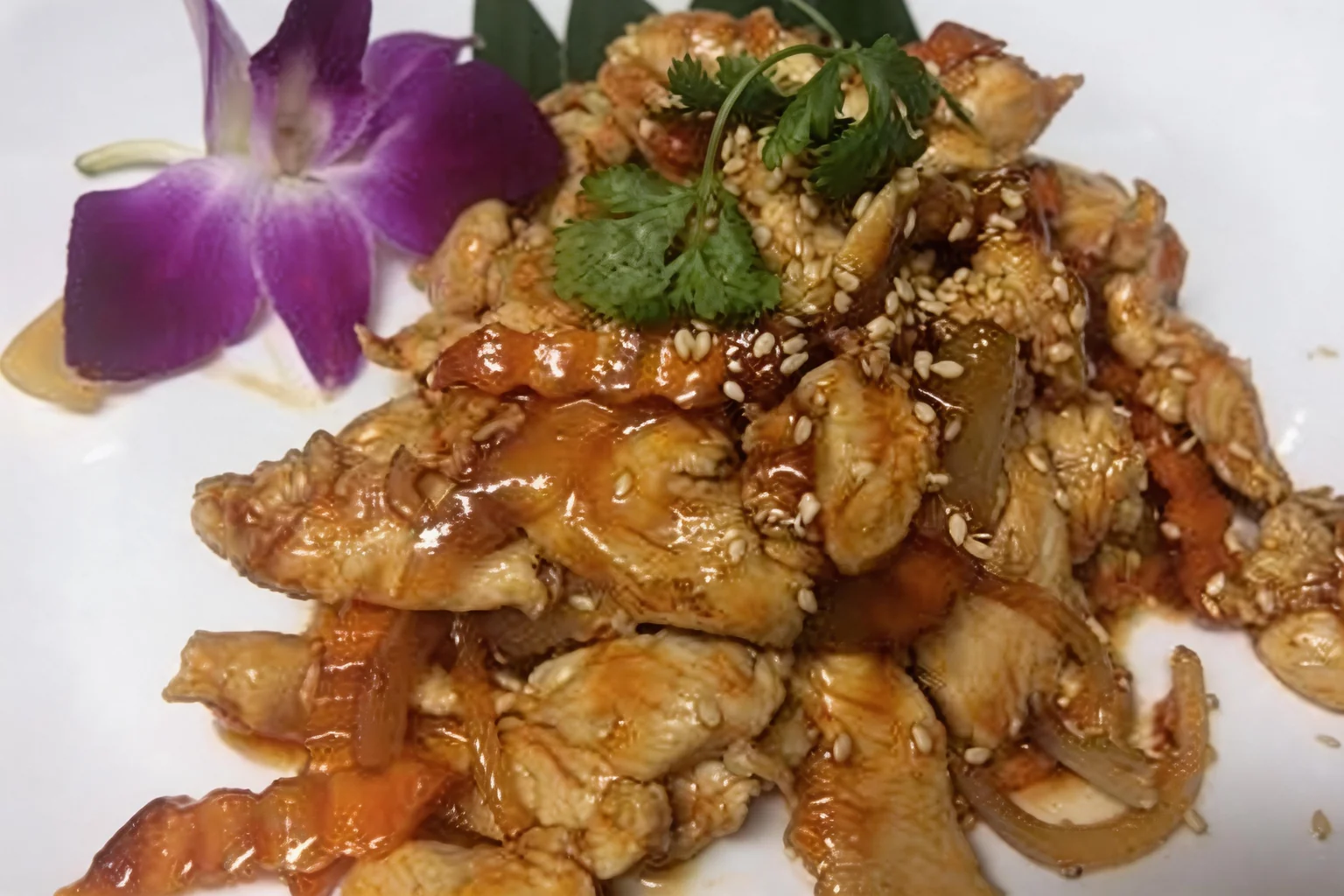 Sautéed chicken on a white plate, purple orchid